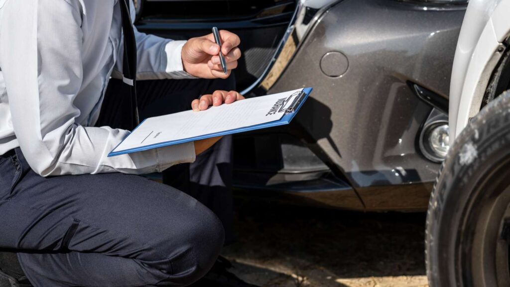 Insurance agent inspecting assessed damaged car checking and signing on report insurance