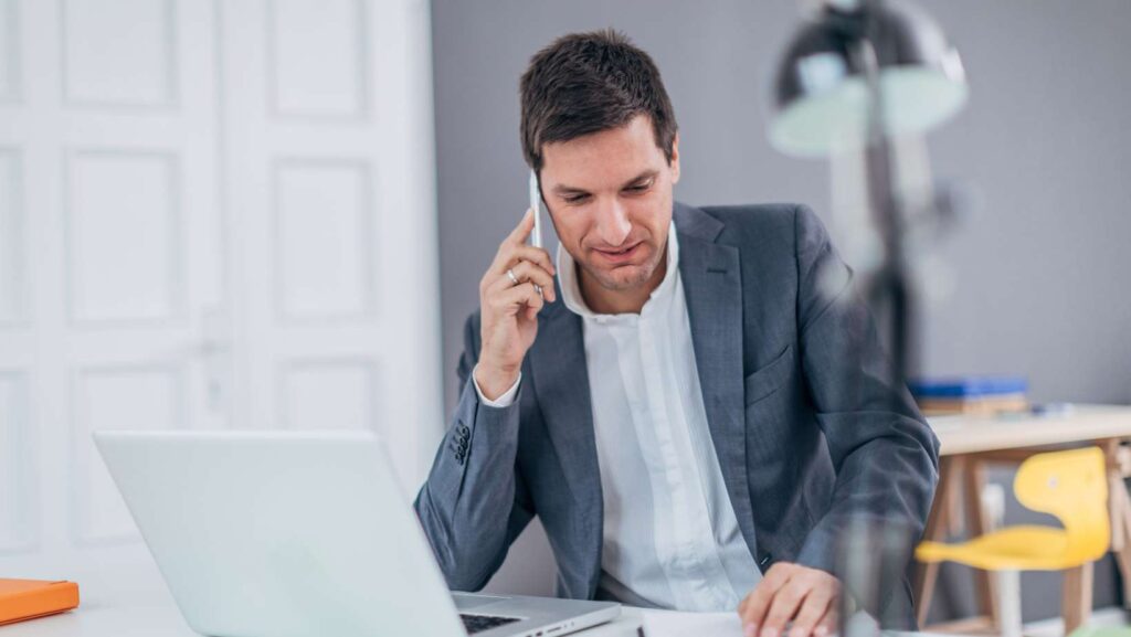 One young  businessman in gray suit, sitting at the office, calling for his shipment company