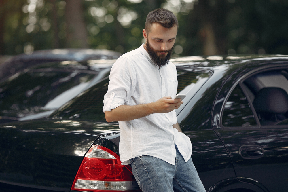 Stylish businessman standing near the car and use mobile phone